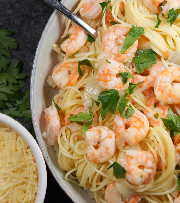 A bowl with noodles, shrimp scampi, onion and parsley. And a small bowl with shredded parmesan.