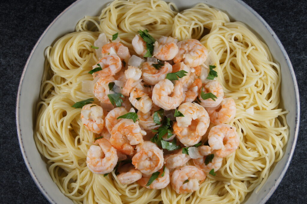 A bowl with noodles, shrimp scampi, onion and parsley.
