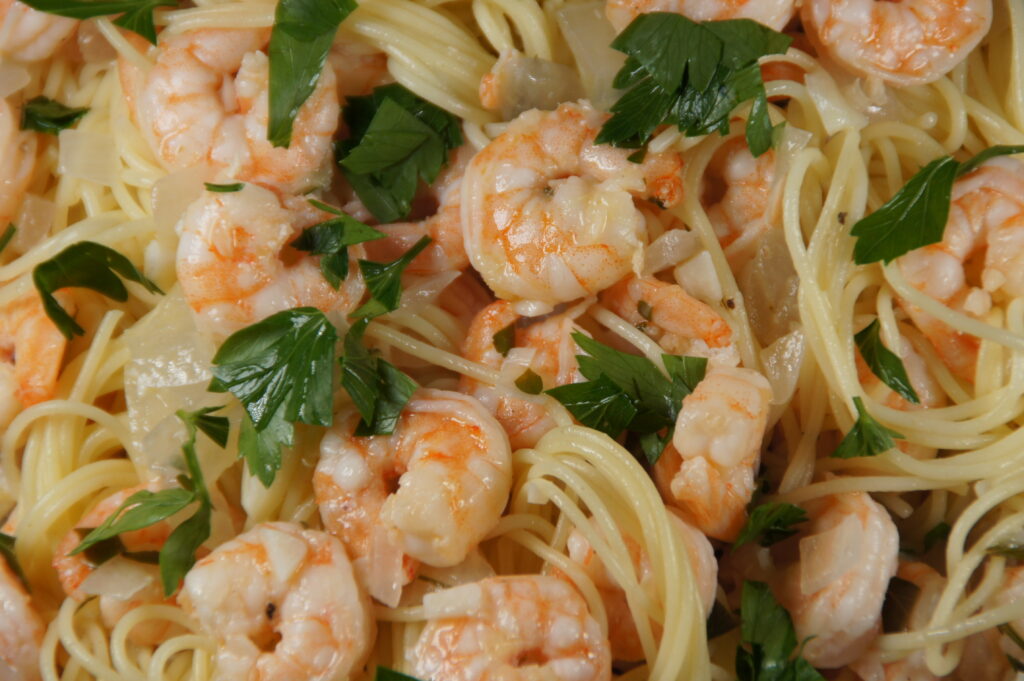 A bowl with noodles, shrimp scampi, onion and parsley.
