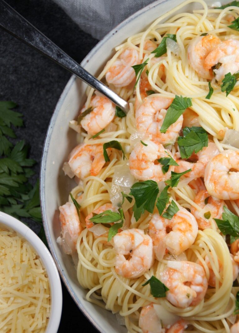 A bowl with noodles, shrimp scampi, onion and parsley. And a small bowl with shredded parmesan.
