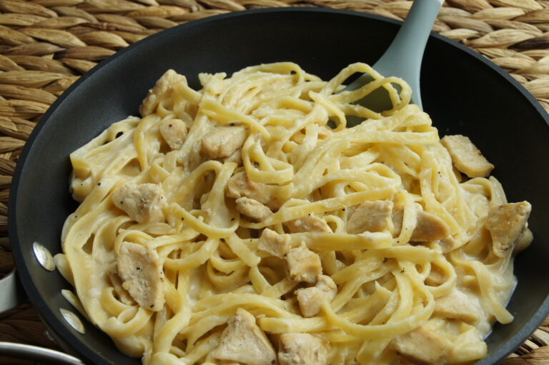 A pan filled with noodles tossed in a lighter, creamy alfredo sauce with chicken.