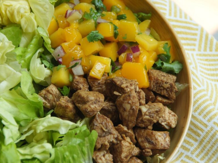 A bowl filled with lettuce, chicken and mango salsa.