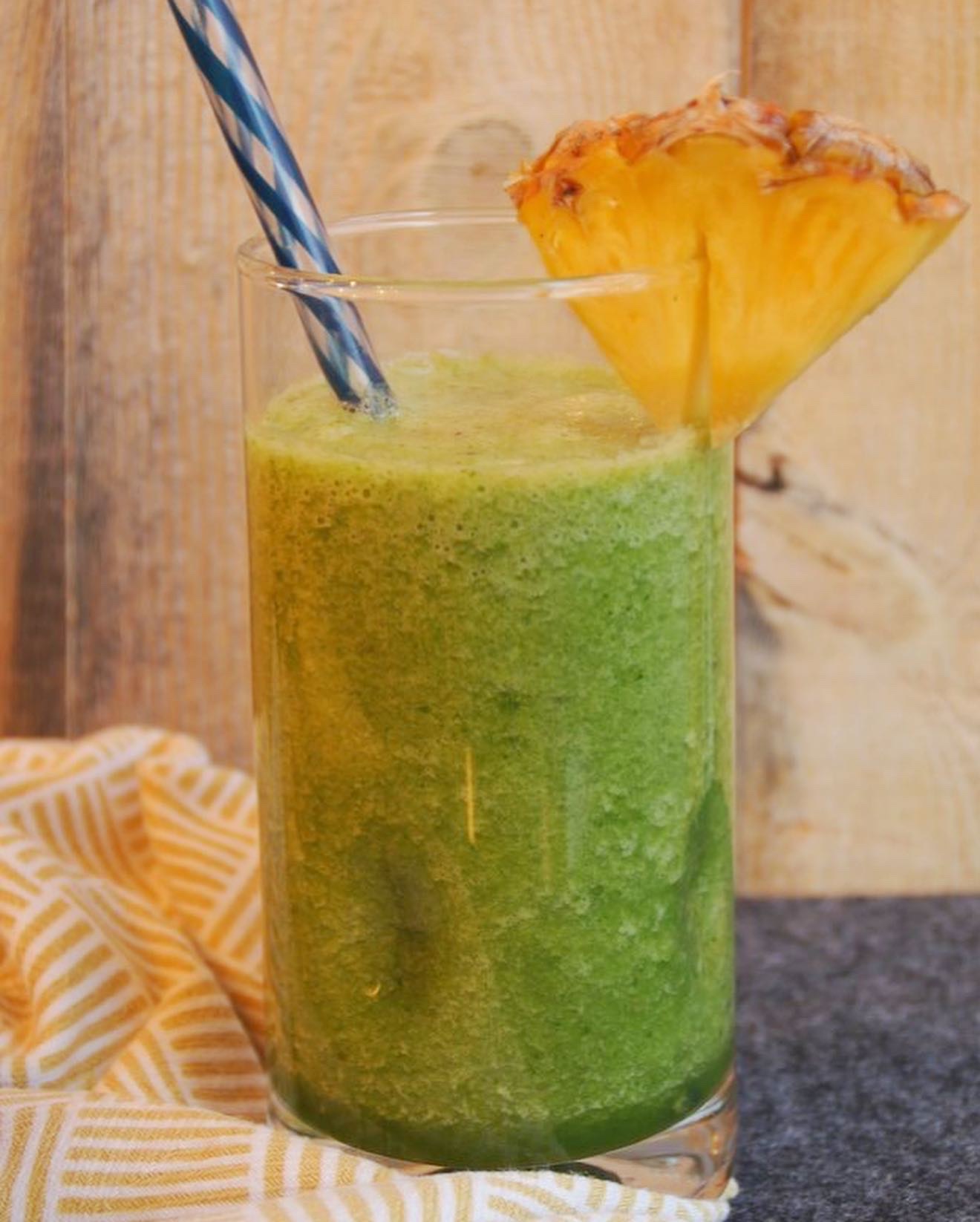 Glass with a green smoothie in it and a pineapple wedge on the side.