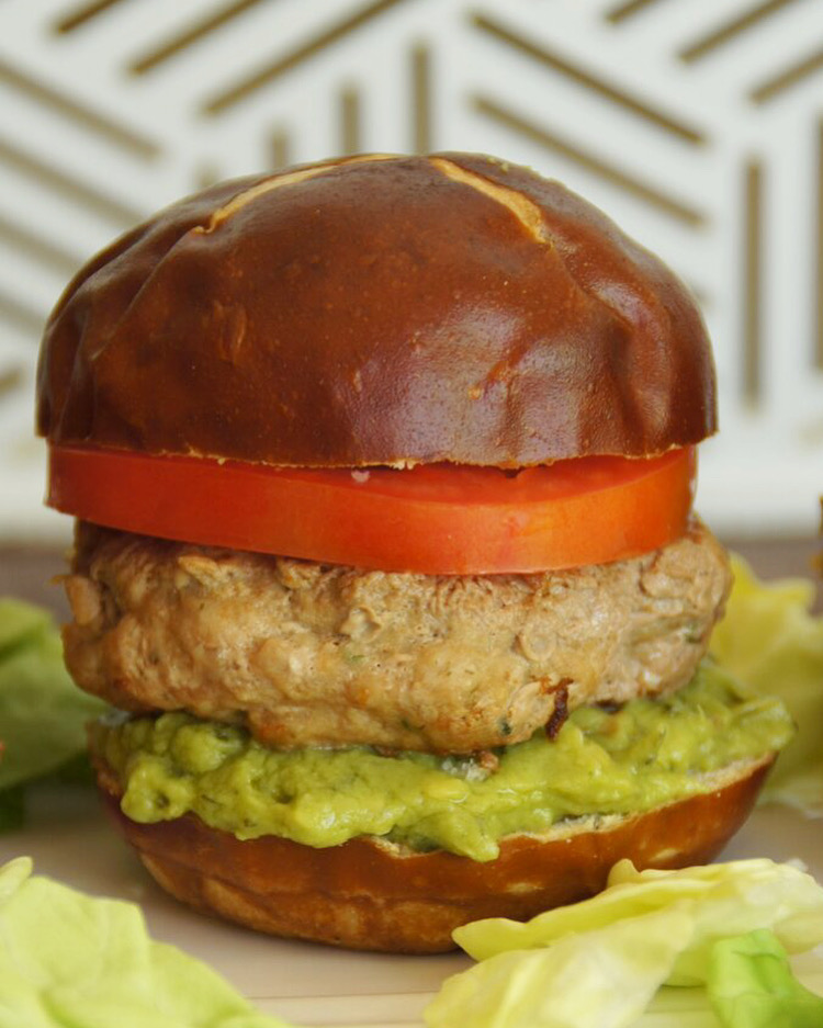 Burger with a pretzel bun, filled with guacamole, a slice of tomato and lettuce