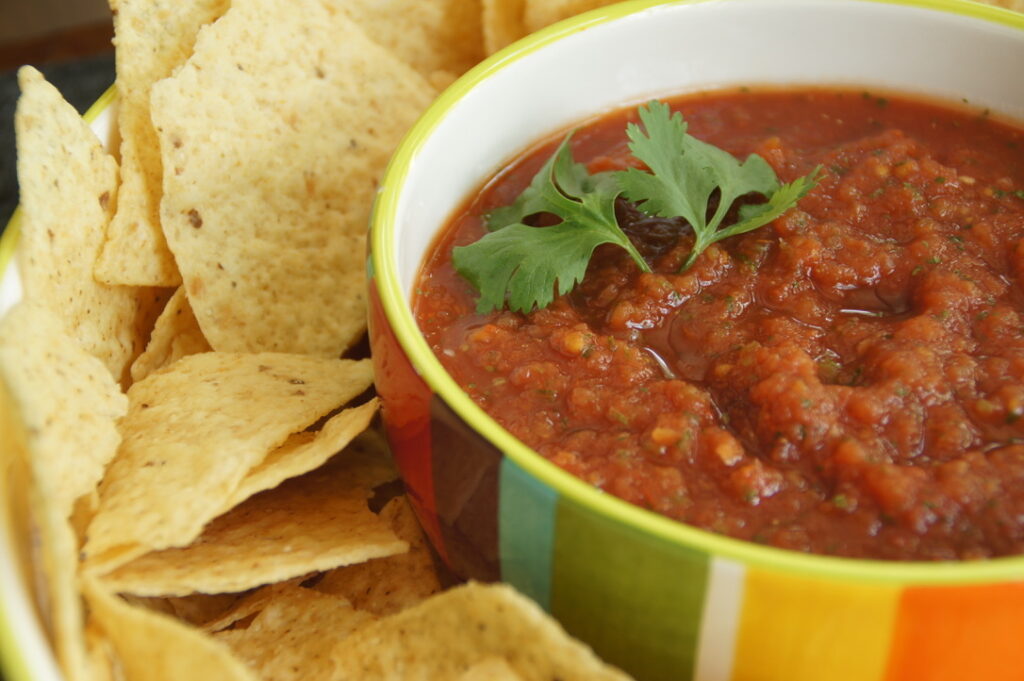 There is a platter of chips and a bowl of red salsa. The salsa is topped with cilantro.
