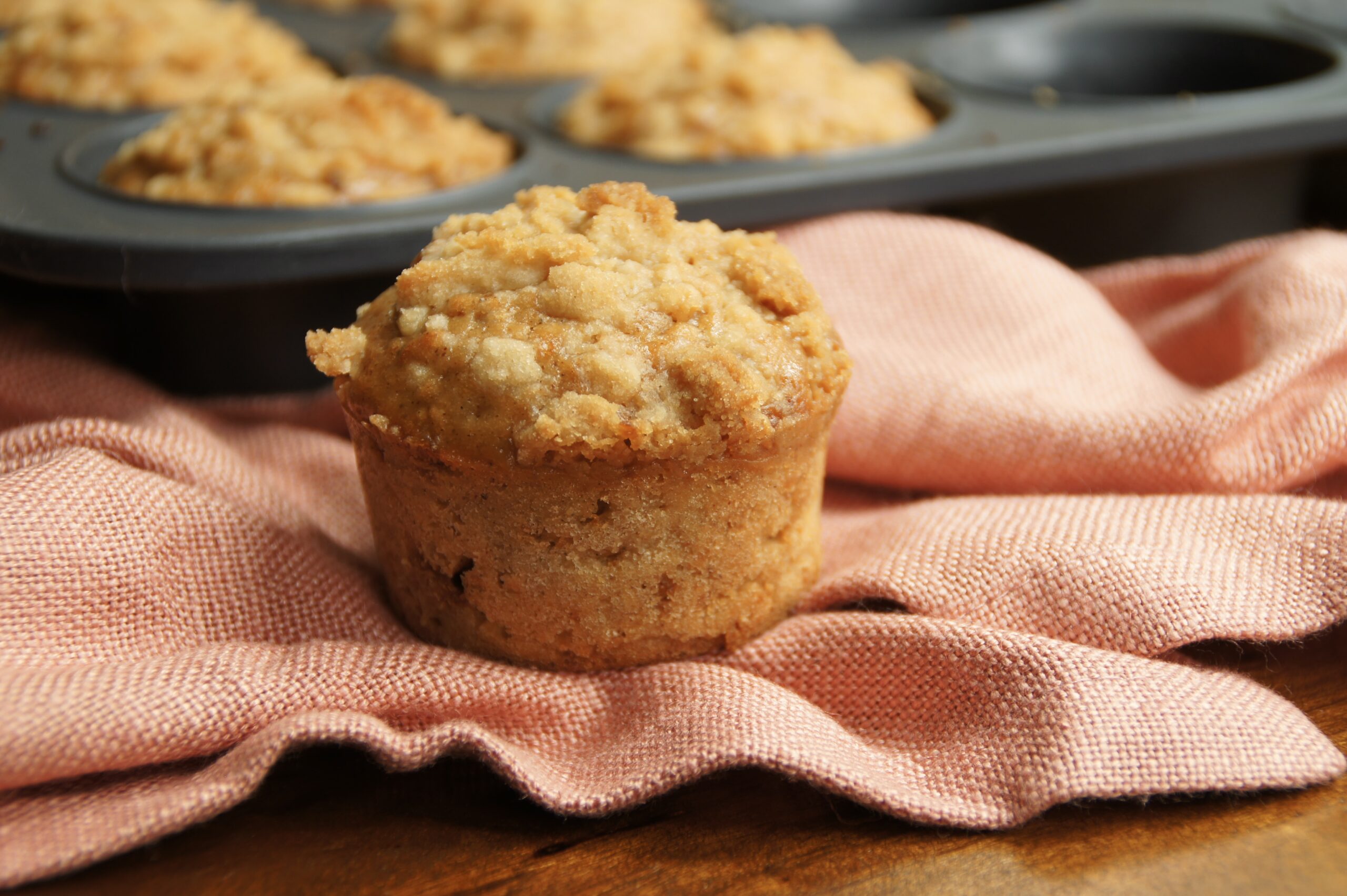 A muffin tray filled with apple cider muffins and an apple on the side.