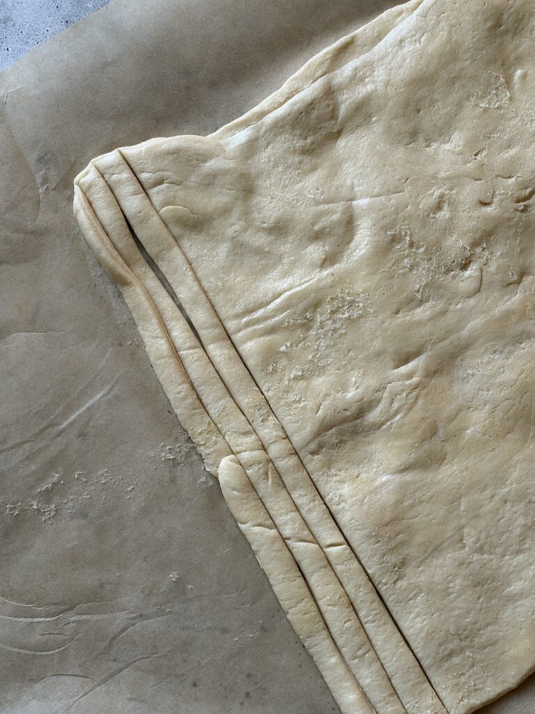 Flaky pastry dough on a piece of parchment paper, cut into thin strips.