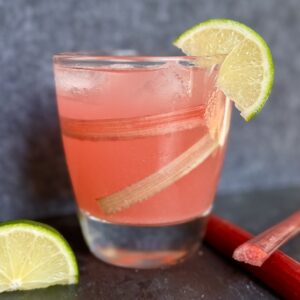 A glass filled with ice and some gin. Topped with tonic water and rhubarb simple syrup. A wedge of lime is on the side.