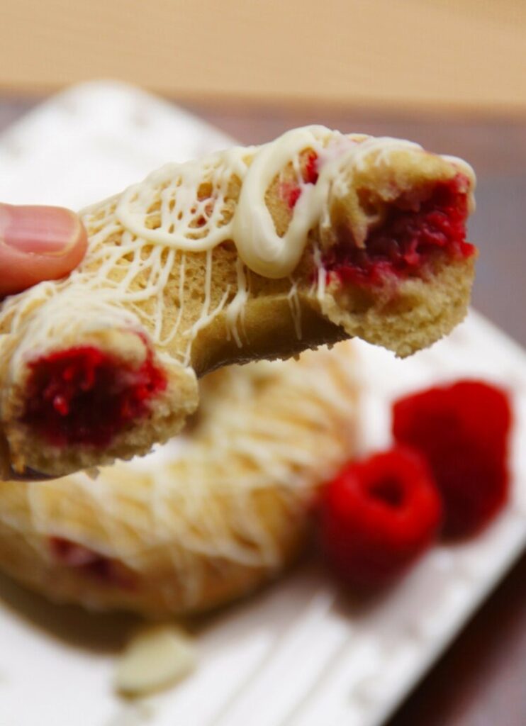 A closeup of a donut filled with fresh raspberries and drizzled with white chocolate.